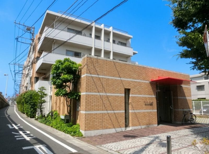 藤沢市　　「猫可」　「猫　不動産」　「猫と幸せに暮らす　売買」　「猫　売買」　「猫可　売買」　「猫可　売買　マンション」　「猫と暮らす　売買」　「猫可物件」　三毛猫ホームズ リノベーション済みの5階建てマンション「びゅうパルク湘南本鵠沼」の外観写真 。落ち着いたタイル張りのデザインに、赤いひさしのエントランスが特徴的で、清潔感のある佇まい 。